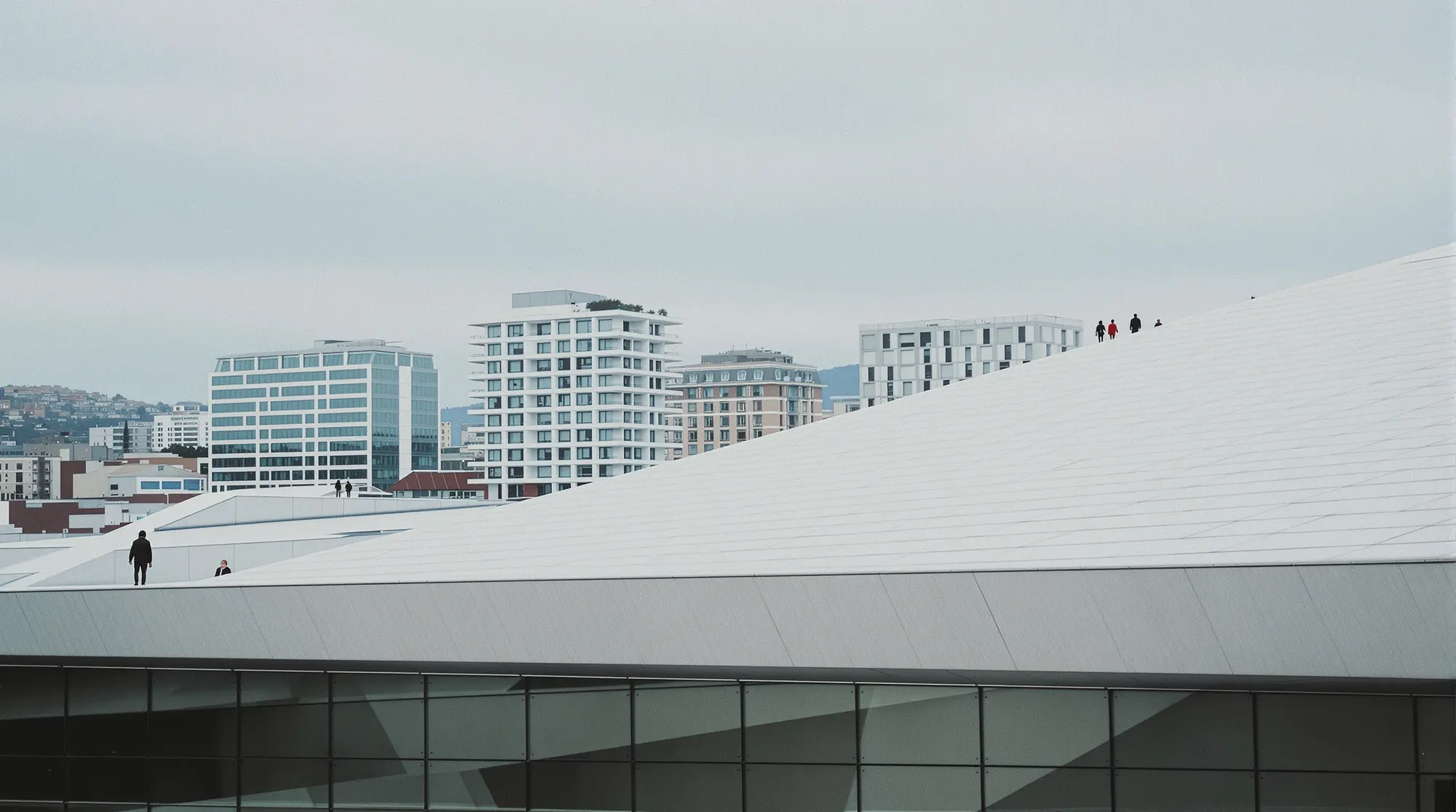 The sloping white roof of the Oslo Opera House, with office buildings in Bjørvika behind it.