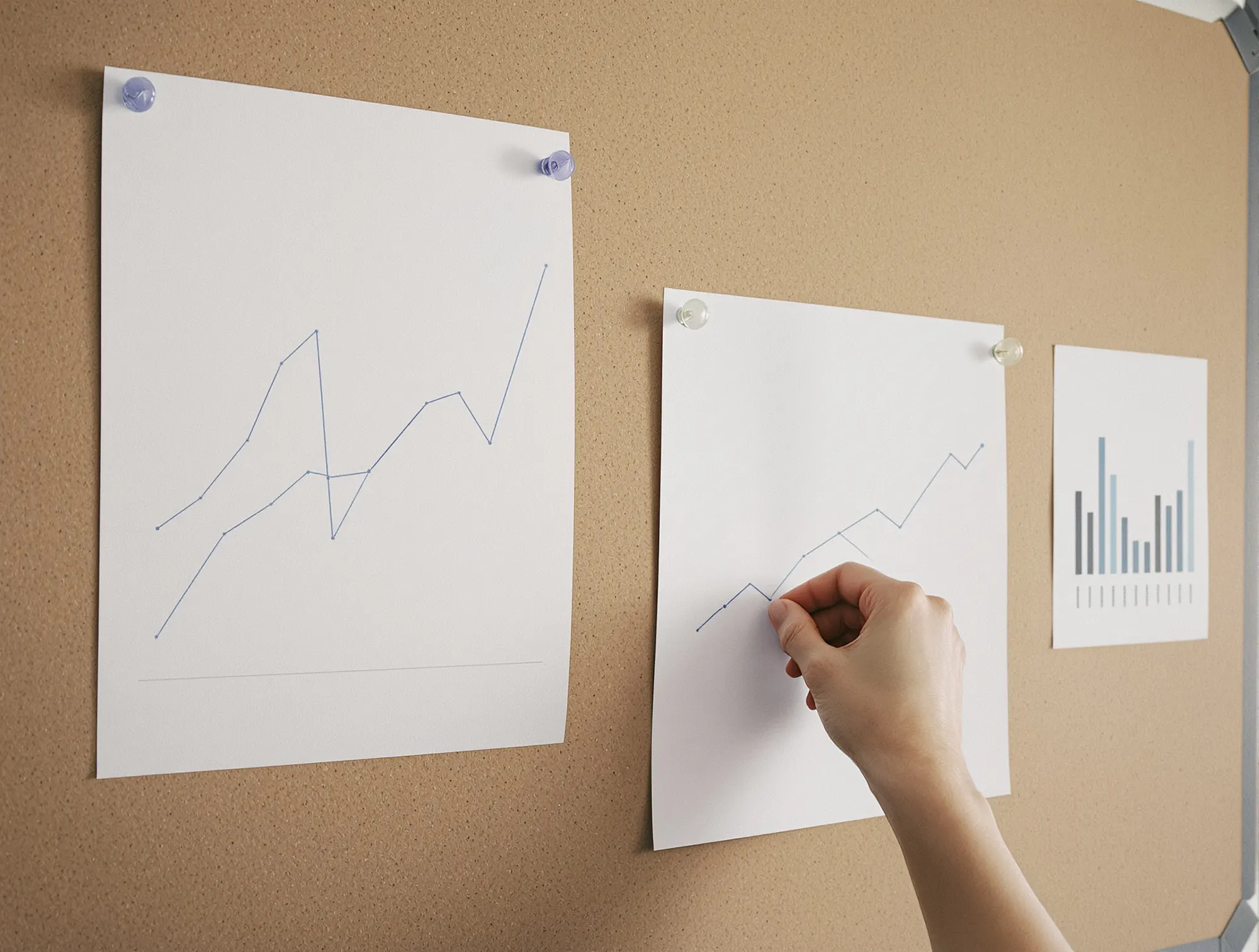 A hand drawing a rising line chart on paper pinned to a cork board